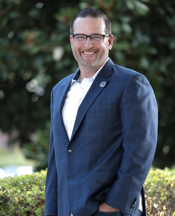 Scott Thompson smiling towards the camera for a corporate headshot in a suit